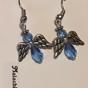 May include: A pair of silver angel wing earrings with light blue crystal beads. The earrings are on a white card with the text "Fashion Jewelry" and "Malachi Kitty Bijoux".