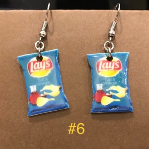 Puede incluir: Un par de pendientes de plata con bolsas de patatas fritas Lay's azules y amarillas. Las bolsas tienen el texto "Lay's" y "Sal & Vinagre".