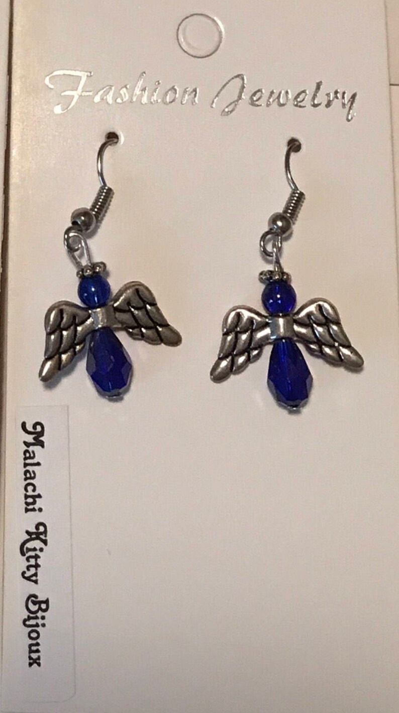 May include: A pair of silver angel wing earrings with blue crystal accents. The earrings are on a white card with the text "Fashion Jewelry" and "Malachi Kitty Bijoux".