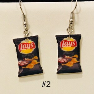 May include: A pair of silver earrings with a black Lay's potato chip bag charm. The bag features the Lay's logo and the text "Barbecue" in white. The earrings are labeled #2.