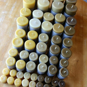 Pu&ograve; includere: Una collezione di candele di cera d'api di diverse dimensioni e tonalit&agrave; di giallo, marrone e beige. Le candele sono disposte a forma di piramide su una superficie di legno.