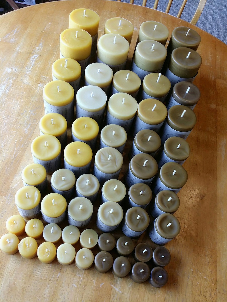 Pu&ograve; includere: Una collezione di candele di cera d'api di diverse dimensioni e tonalit&agrave; di giallo, marrone e beige. Le candele sono disposte a forma di piramide su una superficie di legno.