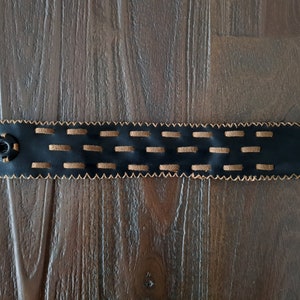 Op de afbeelding: Een zwarte leren armband met bruine stiksels en een metalen knoopsluiting.