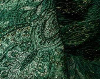 May include: Green fabric with a gold paisley pattern. The fabric has a textured, woven look.