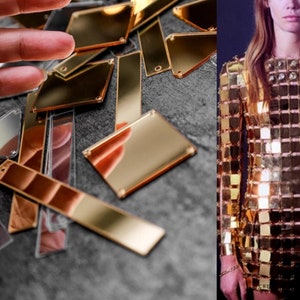 May include: A close-up of gold-toned mirror tiles, some square and some rectangular, scattered on a gray surface.  A woman is wearing a gold dress made of similar tiles.
