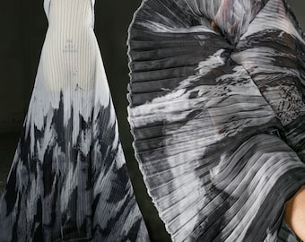 May include: Black and white pleated fabric with a marbled pattern. The fabric is draped over a mannequin and folded in a fan shape.