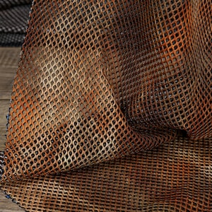 May include: A piece of fabric featuring a diamond-shaped mesh pattern. The material displays a gradient color transition, shifting from a deep black at the edges to a vibrant, rusted orange and brown hue across the center of the textured surface.
