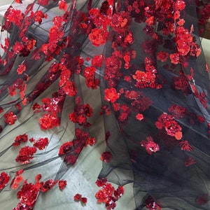 Può includere: Ricamo floreale di paillettes rosse su tessuto a rete nero. Le paillettes sono disposte a forma di fiore e sono sparse sul tessuto.