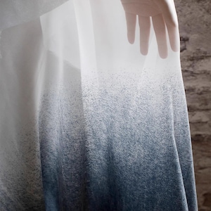 May include: A sheer white fabric with a gradient pattern that transitions from white to dark blue. The fabric is draped over a surface and has a textured appearance.