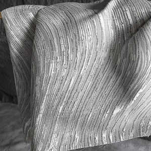 Tejido brocado gris plateado con líneas irregulares, material brillante texturizado para tapicería y vestuario.