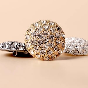 Può includere: Tre bottoni rotondi con finitura dorata e argentata. Ogni bottone è ricoperto di piccoli strass trasparenti.