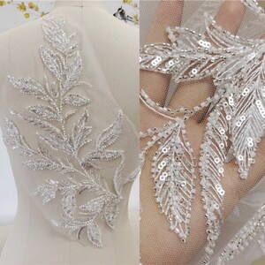 Könnte beinhalten: Eine zarte weiße Blumenapplikation mit silbernen Perlen und Pailletten. Die Applikation ist perfekt, um Brautkleidern, Braut-Accessoires oder anderen Kleidungsstücken für besondere Anlässe einen Hauch von Eleganz zu verleihen.