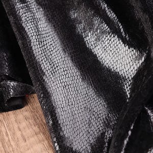 Peut inclure: Gros plan sur un tissu noir avec un motif texturé en forme de filet. Le tissu semble être superposé, avec une surface brillante et réfléchissante sur une couche plus mate en forme de filet. Le fond est une surface en bois brun clair.