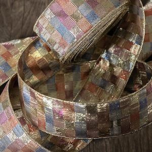 May include: A roll of decorative ribbon with a gold metallic sheen. The ribbon features a woven pattern of squares in shades of gold, blue, red, and purple. The ribbon is ideal for gift wrapping or crafting.