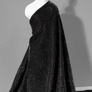 May include: Black velvet fabric with a subtle sparkle. The fabric is draped over a mannequin and has a soft, luxurious feel.