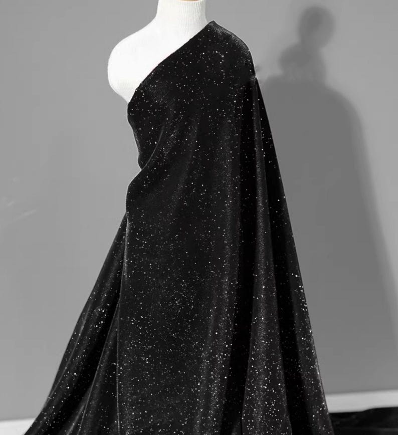 May include: Black velvet fabric with a subtle sparkle. The fabric is draped over a mannequin and has a soft, luxurious feel.