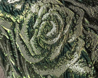 May include: Detailed close-up of a fabric with a raised floral pattern. The material displays a rose design in shades of green and silver, with shimmering metallic threads. The overall effect is luxurious and detailed, suitable for evening wear.