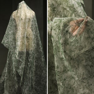 May include: Green and white sheer fabric with a floral pattern. The fabric is draped over a mannequin.