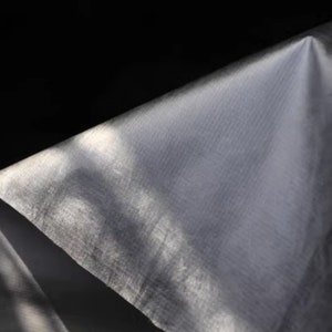 May include: A close-up of a white, textured fabric with a slight sheen. The fabric is folded and draped, creating soft folds and shadows.