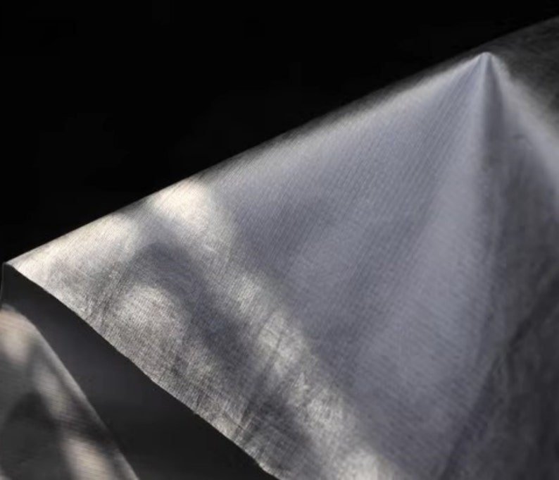 May include: A close-up of a white, textured fabric with a slight sheen. The fabric is folded and draped, creating soft folds and shadows.