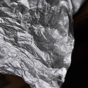 May include: A crumpled sheet of silver foil with a textured surface.