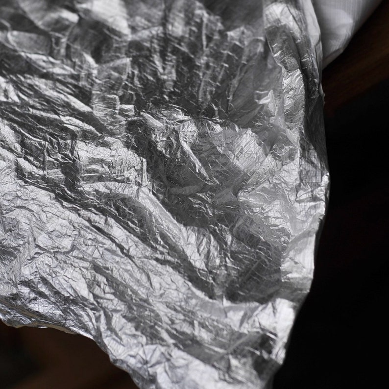 May include: A crumpled sheet of silver foil with a textured surface.