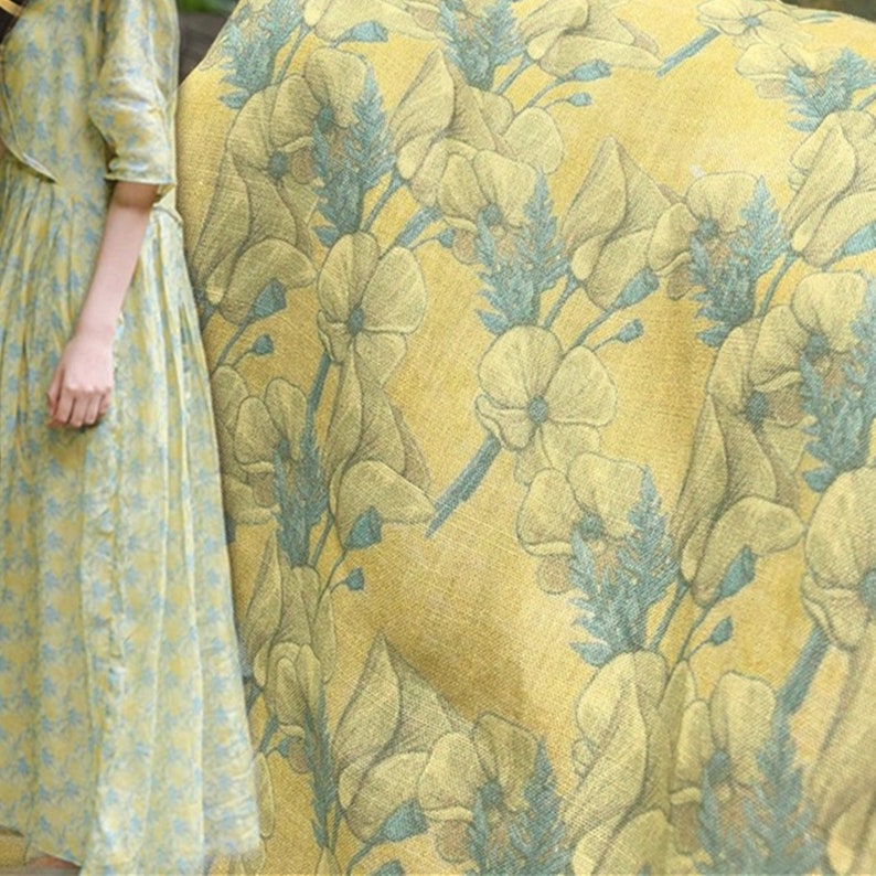 May include: Yellow fabric with a floral pattern featuring blue and yellow flowers. The fabric has a textured linen look.