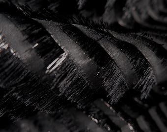 Puede incluir: Primer plano de tela negra con un diseño texturizado y en capas. La tela tiene un patrón acanalado con detalles plumosos y con flecos. El material parece brillante y reflectante, con sutiles variaciones de tono.