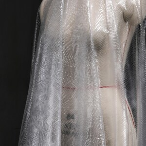 May include: A sheer white fabric with a snakeskin pattern. The fabric is draped over a dress form.