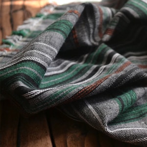 May include: A close-up of a black, green, and white striped fabric with a subtle orange stripe. The fabric is folded and has a soft, textured appearance.