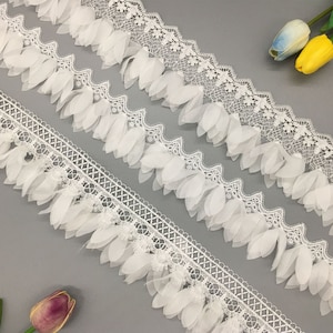 Op de afbeelding: Drie witte kantversieringen met delicate bloemvormige versieringen. De versieringen zijn in een verspringend patroon op een grijze achtergrond gerangschikt.