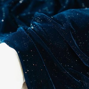 May include: Close-up of a dark blue velvet fabric with a subtle sparkle. The fabric has a soft, luxurious feel and is perfect for creating elegant garments or home decor.