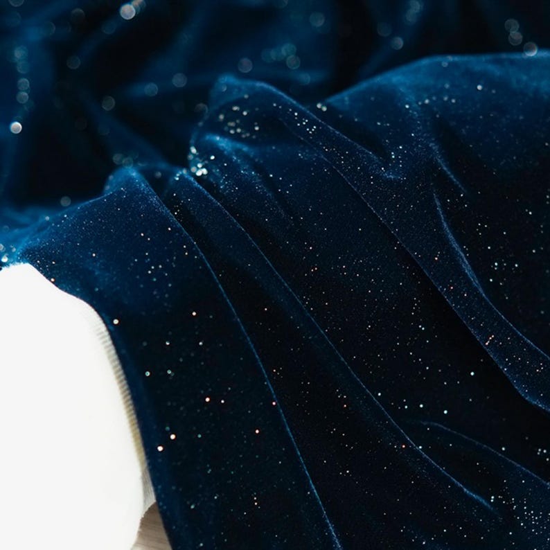 May include: Close-up of a dark blue velvet fabric with a subtle sparkle. The fabric has a soft, luxurious feel and is perfect for creating elegant garments or home decor.