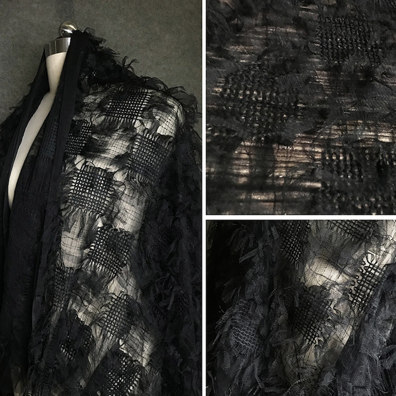 May include: Black sheer fabric with a textured, floral design. The fabric has a delicate, almost feathery texture.