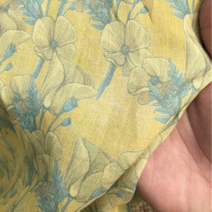 May include: Yellow fabric with a floral pattern. The flowers are light blue and white with a yellow background.