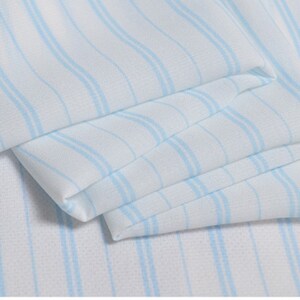 May include: White fabric with thin blue stripes. The fabric is folded and has a soft, flowing texture.
