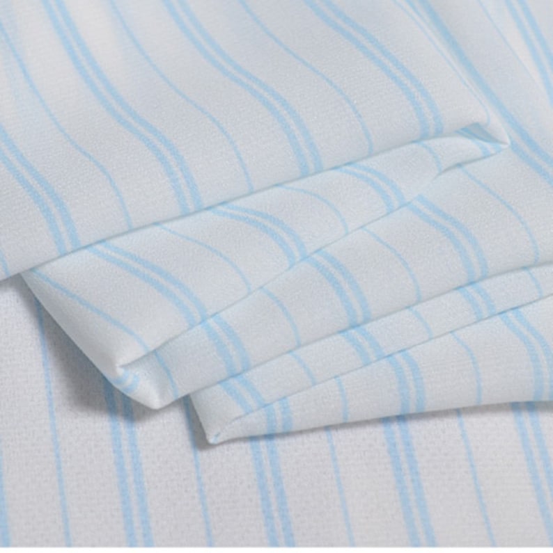 May include: White fabric with thin blue stripes. The fabric is folded and has a soft, flowing texture.