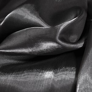 May include: Close-up of a black, shiny fabric with a smooth, silky texture. The fabric is draped and folded, creating soft, flowing lines.