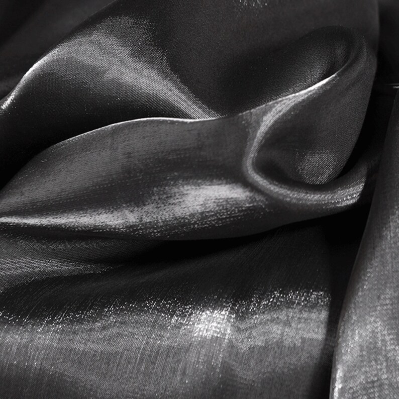 May include: Close-up of a black, shiny fabric with a smooth, silky texture. The fabric is draped and folded, creating soft, flowing lines.