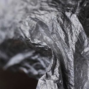 May include: Close-up of a crumpled, silver-colored fabric with a textured surface.