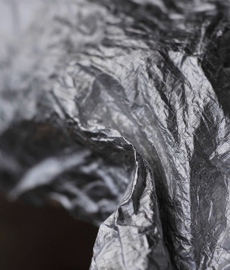 May include: Close-up of a crumpled, silver-colored fabric with a textured surface.