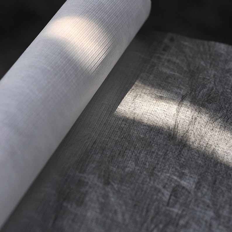 May include: A roll of white fabric with a textured surface is partially unrolled, revealing a roll of black fabric with a similar texture.