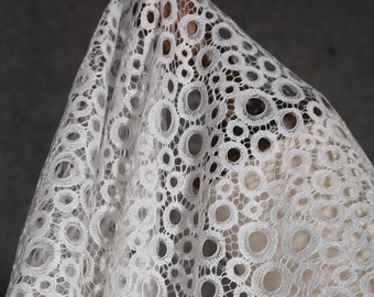 May include: White lace fabric with a circular pattern. The lace is delicate and has a soft, flowing texture.