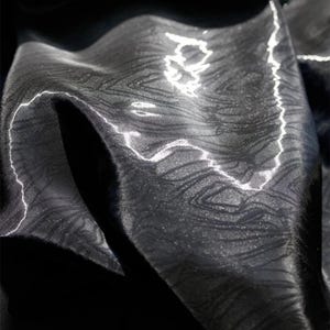 Puede incluir: Primer plano de una tela negra con un patrón sutil y texturizado. La tela es brillante y refleja la luz, creando un efecto brillante.