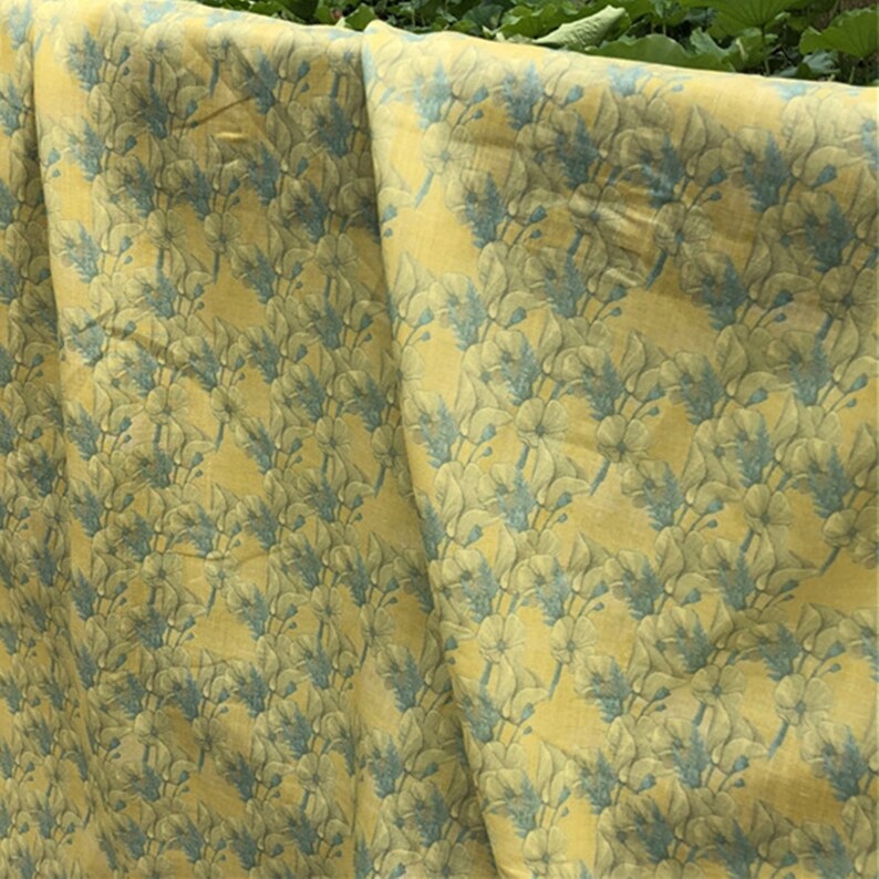 May include: Yellow fabric with a blue floral pattern. The fabric is folded in half and the pattern is visible on both sides.
