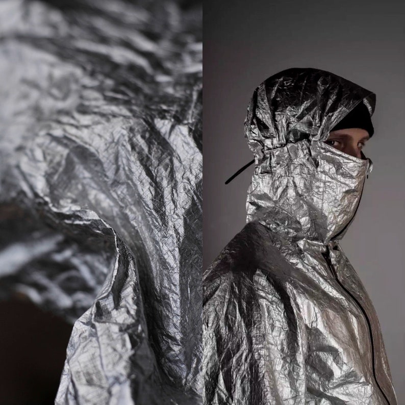 May include: A silver jacket with a hood that is pulled up over the head. The jacket is made of a crinkled material and has a zipper closure.