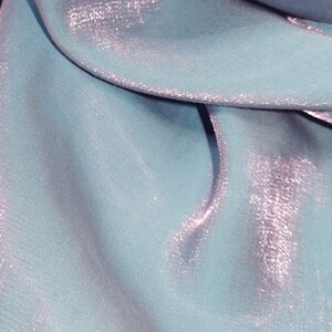 May include: A light blue fabric with a subtle shimmery finish. The fabric is folded and draped, showcasing its texture and sheen.
