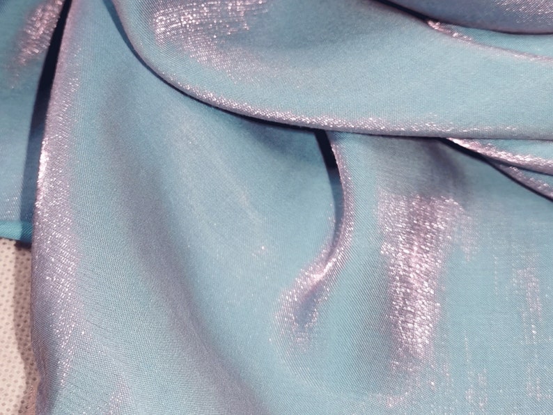May include: A light blue fabric with a subtle shimmery finish. The fabric is folded and draped, showcasing its texture and sheen.