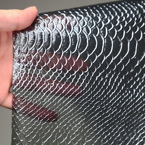 May include: A close-up of a black snakeskin-embossed leather sheet. The leather has a glossy finish and a textured surface.