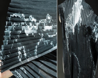 May include: Black pleated fabric with a white marble pattern. The fabric is folded in a fan shape.